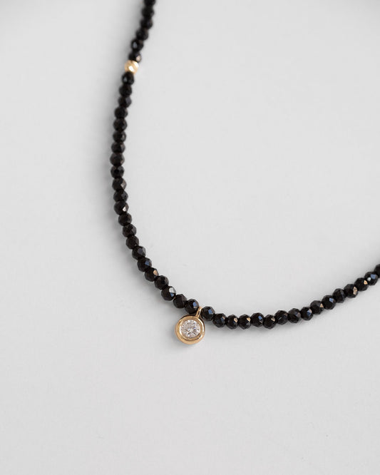 gold beaded necklace with black spinel stones and single diamond in the middle